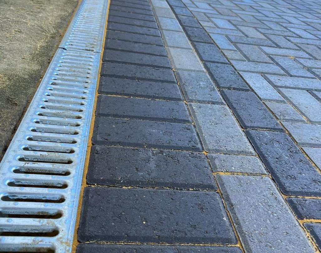 Close up of a channel drain set flush against the block paving edge course
